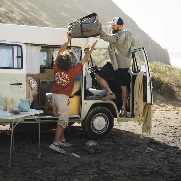 Zwei Männer mit einer Reisetasche vor einem Camping-Van