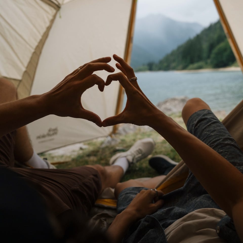 Zwei Personen liegen in einem Zelt und formen mit ihren Händen gemeinsam ein Herz